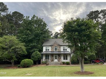 Charming two-story home with a stone and vinyl facade, surrounded by mature trees and lush landscaping at 7501 Tipsy Sq, Wake Forest, NC 27587
