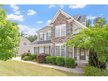 Charming two-story home featuring a stone facade, gray siding, manicured lawn, and lush landscaping at 113 Old Ballentine Way, Holly Springs, NC 27540