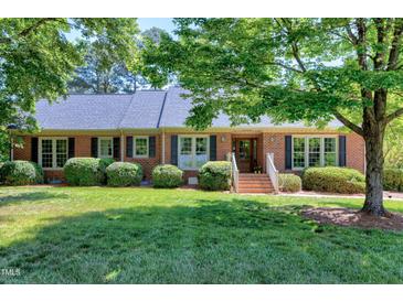 Charming brick home featuring a lush green lawn, mature trees, and classic shutters at 7204 Bellweather N Ct, Raleigh, NC 27615
