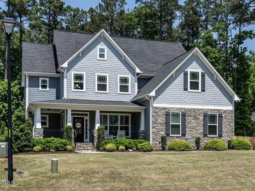 Charming two-story home with a combination of stone and gray siding, complemented by lush landscaping at 497 Rockport Dr, Clayton, NC 27527