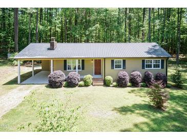Charming single-story home with a metal roof, cozy front porch, and well-manicured landscaping in a wooded setting at 4221 River Run Dr, Sanford, NC 27332