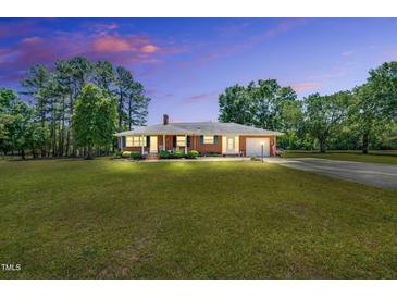 Charming brick ranch-style home with well-manicured lawn and mature trees against a beautiful colorful sunset sky at 585 Cokesbury Rd, Fuquay Varina, NC 27526