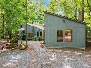 Charming exterior of a home surrounded by lush greenery and trees, with a gravel driveway at 61 Stone Ledge, Pittsboro, NC 27312