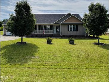 Charming single-story home featuring a covered porch and a well-manicured lawn with mature trees and landscaped features at 59 Long Grass Dr, Smithfield, NC 27577