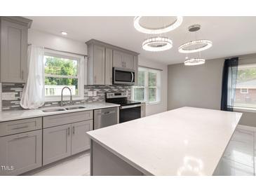 Modern kitchen features stainless steel appliances, grey cabinets, mosaic backsplash and island with white countertop at 2315 Oxford Rd, Henderson, NC 27536