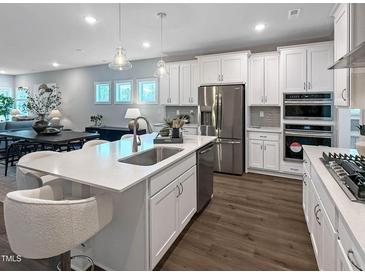 Bright kitchen boasts white cabinets, stainless steel appliances, and a large island with counter seating at 87 Addison Pond Ct, Zebulon, NC 27597