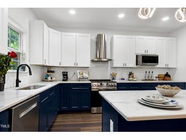 Modern kitchen featuring white cabinets, stainless steel appliances, and a stylish island with marble countertops at 2003 Pilot Mountain Ct, Apex, NC 27502