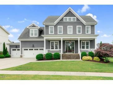 Beautiful gray two-story home featuring a large front porch, well-manicured lawn, and attached two-car garage at 320 Chickasaw Plum Dr, Holly Springs, NC 27540