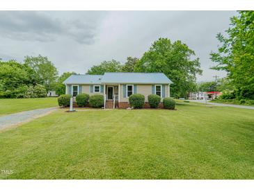 Charming home features a bright blue metal roof and lovely, well-maintained landscaping at 403 Rolling Rd, Haw River, NC 27258