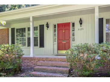 Charming home entrance featuring a bright red door with sidelights and classic black sconces at 3125 Stanford Dr, Durham, NC 27707