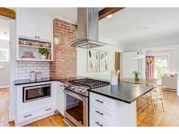 Modern kitchen with stainless steel appliances, white cabinetry, and brick accent wall over a hardwood floor at 800 E Forest Hills Blvd, Durham, NC 27707