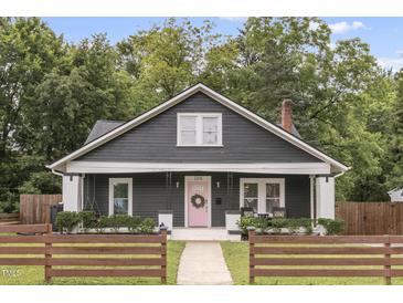 Charming one-story home featuring a pink front door and a cozy front porch, all surrounded by lush greenery and a lovely wood fence at 106 E Delafield Ave, Durham, NC 27704