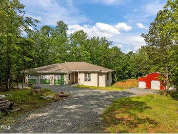 Charming home with a gravel driveway, lush green trees and red barn on a sunny day at 121 Pheasant Ct, Pittsboro, NC 27312