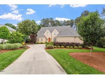 Beautiful brick home with lush green lawn, mature trees and long driveway on a partially cloudy day at 8904 Milden Hall Ct, Raleigh, NC 27615