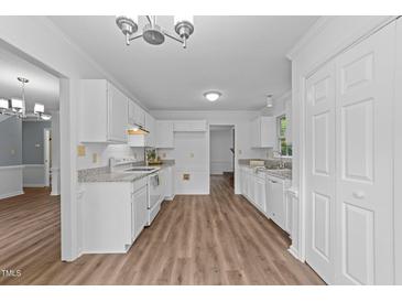 Bright kitchen features white cabinetry, granite countertops, and wood-look flooring at 5401 Lower Creek Ct, Apex, NC 27539