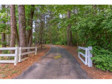 Long, winding driveway through lush woods with white fencing at the entrance at 117 Carolina Forest Rd, Chapel Hill, NC 27516