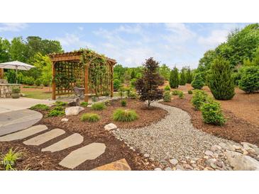 Beautiful backyard with stone walkway, mulch, and wooden pergola covered in climbing vines and surrounding greenery at 829 Churton Pl, Cary, NC 27518