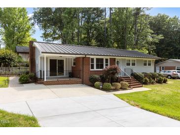 Charming one story home with a metal roof, brick and gray siding and mature landscaping at 203 W Boundary St, Cary, NC 27513