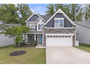 Charming two-story home with stone accents, a two-car garage, a blue front door, and mature landscaping at 4001 Bostwyck Dr, Fuquay Varina, NC 27526