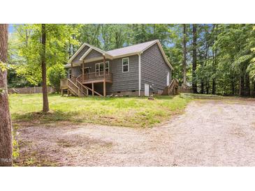 View of the side and rear of the house showing the wooden porch, gravel driveway, and lush trees at 1027 Holden Rd, Youngsville, NC 27596