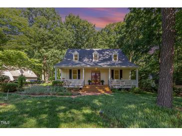 Charming home with a welcoming front porch, brick walkway, and surrounded by lush greenery and trees at 9417 Greenfield Dr, Raleigh, NC 27615