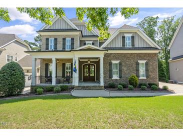 Charming brick home featuring a covered front porch, manicured lawn, and mature landscaping at 117 Synandra Ln, Holly Springs, NC 27540