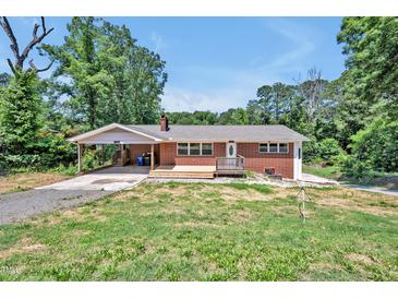 Charming brick home featuring a carport and a wooden porch, surrounded by a partially wooded lot at 112 S Joyland St, Durham, NC 27703