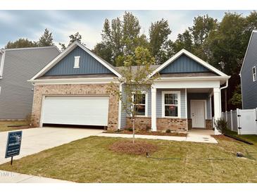 Charming, single-story home boasts a brick and blue facade, complemented by a well-manicured lawn and attached garage at 124 N Keatts Winner Ct, Wilson's Mills, NC 27520