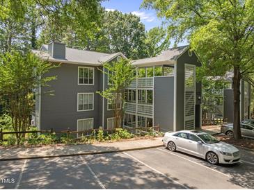 Three-story gray condo building featuring wood trim, a parking lot, and surrounded by mature trees at 4631 Timbermill Ct # 203, Raleigh, NC 27612