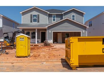 Unfinished two-story home featuring gray siding and an open garage with construction equipment and a portable toilet at 744 Deschutes Dr, Garner, NC 27529