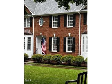 Charming brick townhouse featuring an arched entrance, black shutters, and a well-manicured lawn at 227 Kenmont Dr, Holly Springs, NC 27540