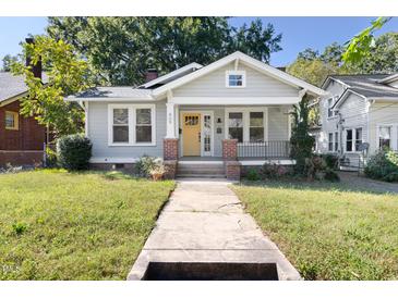 Charming single-story home featuring a quaint front porch, bright yellow door, and beautifully maintained yard at 409 N Hyde Park Ave, Durham, NC 27703