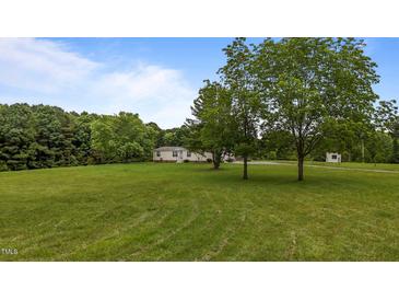 View of the property's green front yard with large trees and a house in the background on a sunny day at 5200 Mrs Fuller Rd, Mebane, NC 27302