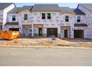 Exterior view of a townhome construction site showing Tyvek HomeWrap, garage doors, and building materials at 1033 Winding Spring Dr, Mebane, NC 27302