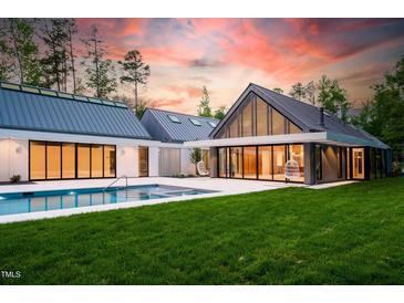 Stunning backyard view showcasing a modern pool, lush green lawn, and contemporary architectural design at sunset at 295 Lystra Preserve Dr, Chapel Hill, NC 27517