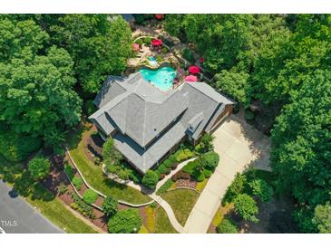 Aerial view of a luxury house with a uniquely shaped pool, red umbrellas, mature trees, and a winding driveway at 4021 Chaumont Dr, Apex, NC 27539
