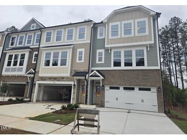 Modern townhome boasts an attached garage, complemented by large windows and brick and siding details at 5028 Jowetts Walk Dr # 24, Cary, NC 27519