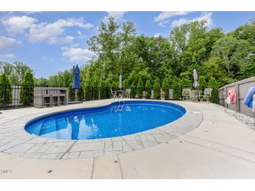 Backyard in-ground pool surrounded by patio, black metal fence, and mature trees offering a private outdoor space at 150 Sherrill Place Ln, Garner, NC 27529