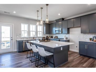 Modern kitchen boasts gray cabinetry, stainless steel appliances, and a large quartz island with pendant lighting at 809 Hyperion Aly, Wake Forest, NC 27587