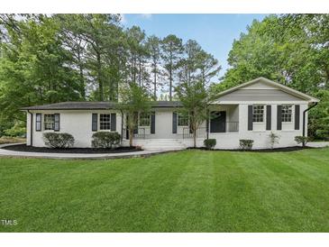 Charming white brick home with black shutters and a beautifully landscaped front yard and mature trees at 132 Edgewood Dr, Louisburg, NC 27549