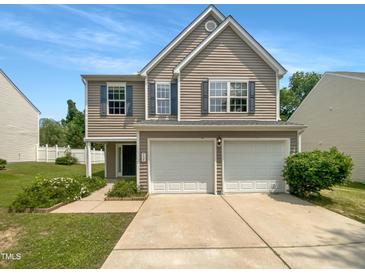 Two-story home with a two-car garage, tan siding, blue shutters, and manicured lawn on a clear day at 735 Sycamore Springs Dr, Fuquay Varina, NC 27526