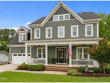 Traditional two-story home with a covered front porch, American flag, green siding, and manicured lawn at 821 Rambling Oaks Ln, Holly Springs, NC 27540