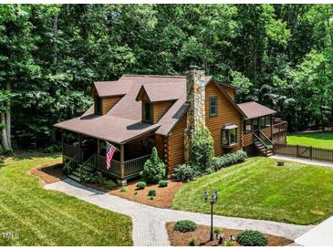 Charming log home with stone chimney, landscaped yard, and inviting front porch with the American flag at 2416 Kearney Rd, Wake Forest, NC 27587