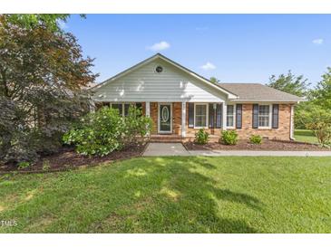 Charming brick home with manicured lawn, flowering bushes, and a covered front porch at 6411 Pondview Ln, Durham, NC 27712