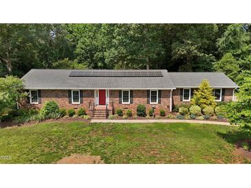 Charming brick ranch home with a red front door, lush landscaping, and solar panels at 825 Whispering Wind Rd, Burlington, NC 27217