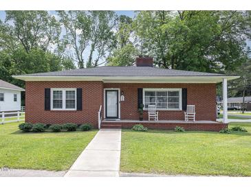 Charming single-story brick home featuring a manicured lawn, front porch with rocking chairs, and inviting curb appeal at 208 S College Ave, Kenly, NC 27542