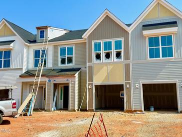 New construction townhomes with various colored siding, bright windows, and attached garages awaiting finishing touches at 87 Ripple Way # 214, Clayton, NC 27520