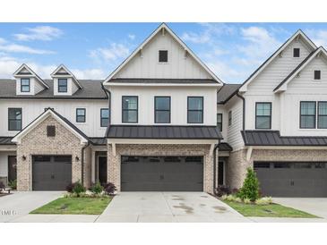 A modern townhouse with white siding, a gray brick facade, a dark garage door, and a well-manicured lawn at 109 Periwinkle Pl, Clayton, NC 27527