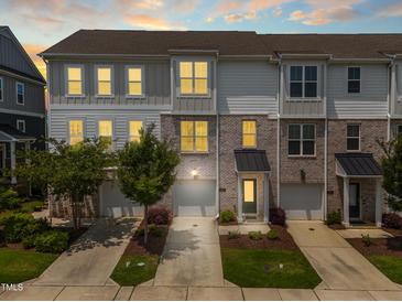 Three-story townhomes showcasing gray, white, and brick exteriors, small trees, and driveways leading to garages at 364 Skymont Dr, Holly Springs, NC 27540