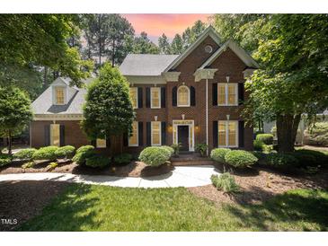 Beautiful brick home with manicured landscaping and a charming front entrance, with a colorful sunset in the background at 5216 Sunset Fairways Dr, Holly Springs, NC 27540